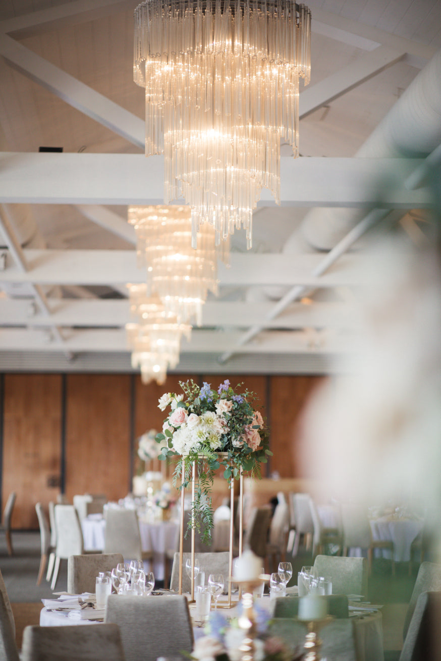 Elegant floral centerpiece with mixed pastel flowers under a grand crystal chandelier in a wedding hall.