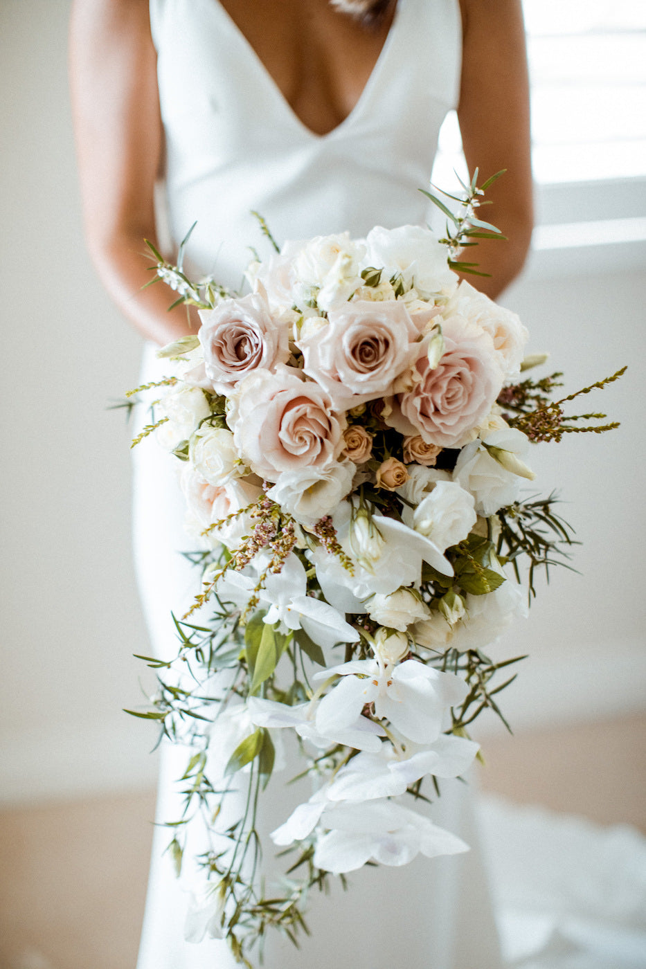 Bride in a white dress holding a large bouquet of white and blush roses with delicate greenery.