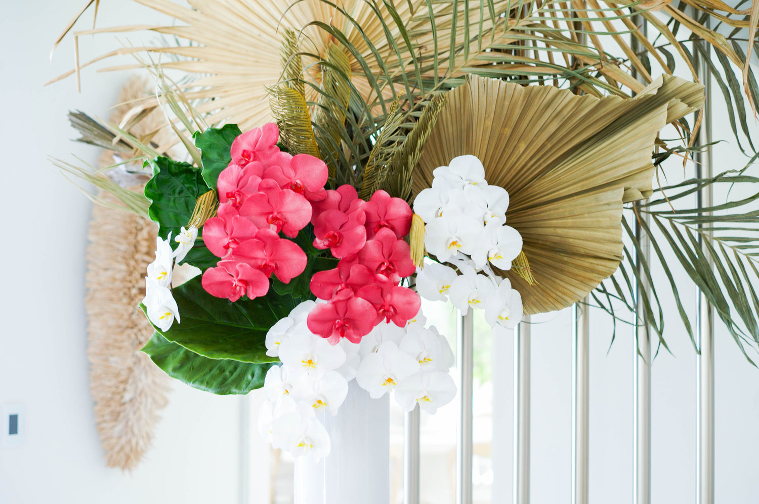 Floral arrangement with pink and white orchids and large dried palm leaves.
