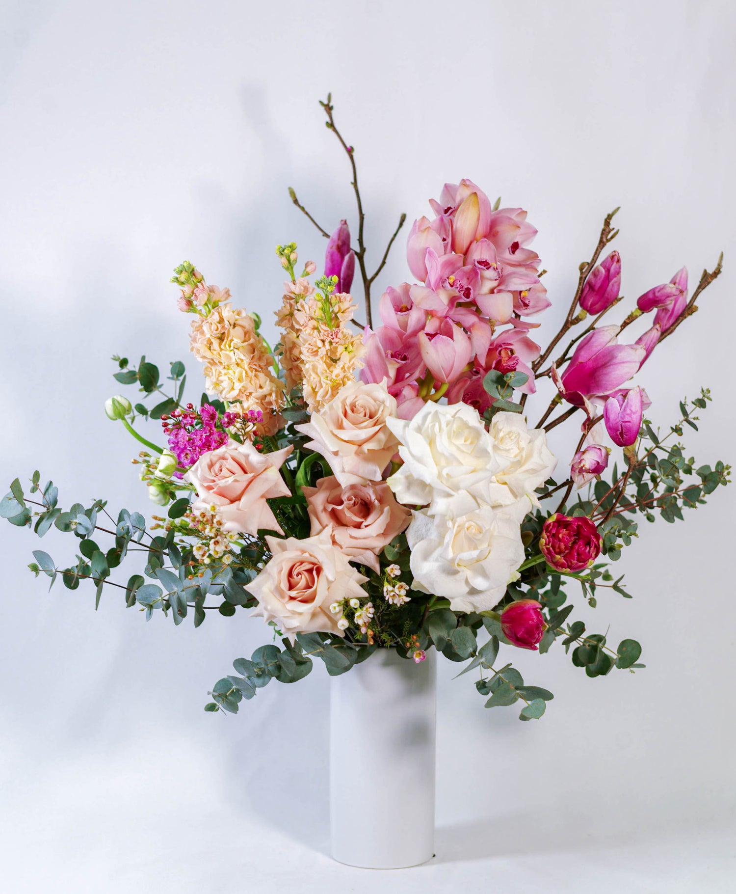 Elegant flower arrangement in a white vase featuring pink, white, and peach roses with eucalyptus leaves.