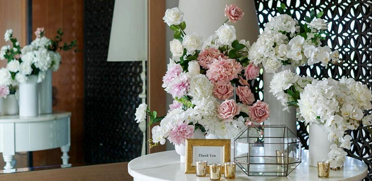 Lush floral arrangement of pink and white flowers on a reception table with complementary decor in the background.