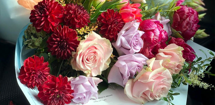 Colorful bouquet of red dahlias, pink roses, and lush greenery on a table with a soft focus background.
