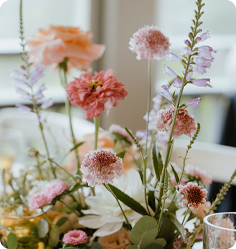 Soft pastel floral arrangement with pink dahlias and delicate purple flowers on a light background.