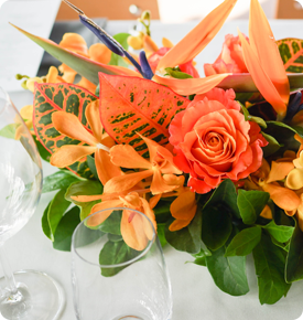 Vibrant floral centerpiece with orange roses and tropical flowers on a dining table.