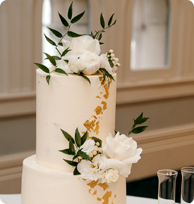 Three-tiered wedding cake decorated with white roses and green leaves, accented with gold leaf.