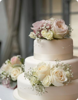 Elegant multi-tiered wedding cake adorned with pink and white roses and delicate baby's breath.