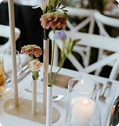 Intimate table setting with white candles and delicate floral arrangements featuring pastel flowers.
