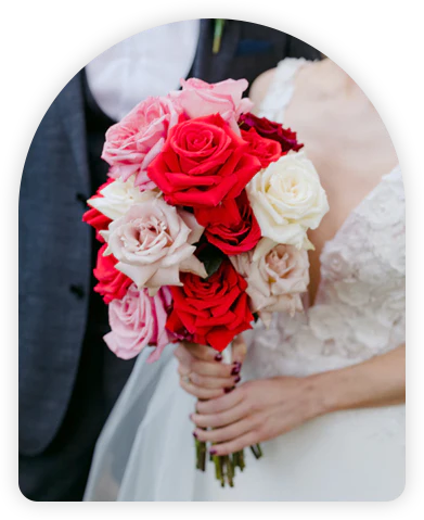 Close-up of a bride holding a vibrant bouquet of red and white roses, symbolizing love and purity.