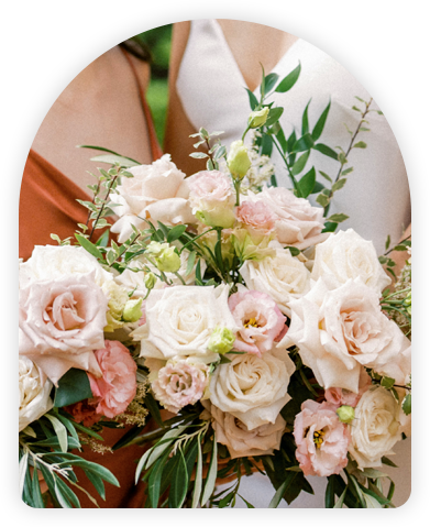 Bridesmaid in a rust-colored dress holding a bouquet of soft pink and white roses surrounded by greenery.