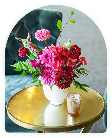 Elegant floral centerpiece with pink dahlias and deep red blooms on a gold side table in a modern setting.