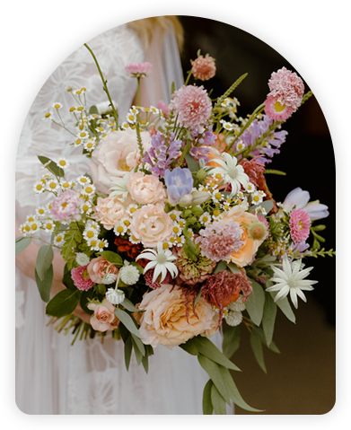 Bride in a flowing gown holding a lush bouquet filled with pink, peach, and white flowers, complemented by delicate greenery.