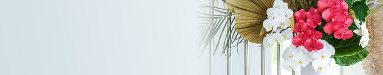 Floral arrangement with pink and white orchids and large dried palm leaves on a light background.