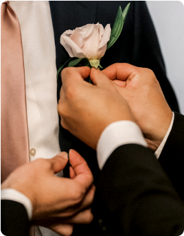 A person pinning a pink rose boutonniere onto a suit jacket.