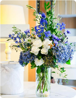 Vase with blue and white flowers on a table, next to a white decorative item.