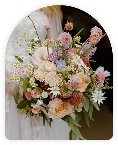 A colorful bridal bouquet with pink, orange, and white flowers held by a bride in a white dress.