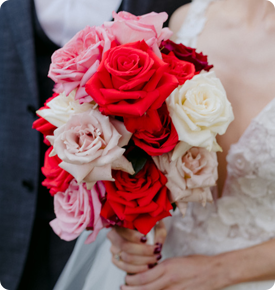 Close-up of a bride holding a bouquet with red and white roses.