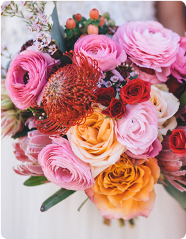 A colorful bridal bouquet with pink, orange, and red flowers.